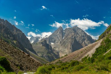 Yükselen engebeli dağlar, dik kayalık yamaçlar, yemyeşil çayırlar, uzak kar tarlaları, manzaralı dağ yollarında yürüyen yürüyüşçüler, canlı yaz atmosferi, el değmemiş vahşi doğa, macera ruhu..