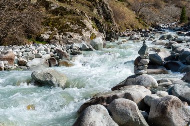 Ala-Archa Parkı, engebeli araziyle çevrili hızlı akan nehir, büyük taşlar. Dengeli kaya cairn, dağcılığın, keşfin ve el değmemiş doğada taşra seyahatinin ruhunu temsil ediyor..