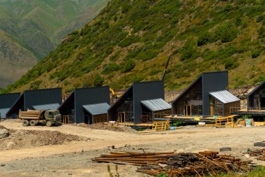 Modern A-frame chalets, eğimli arazi üzerine inşa edilen İskandinav evleri, stilt temeller. İnşaat araçları ve malzemeler. Dağlara kurulmuş, dağ turizmi ve tatil için tasarlanmış..
