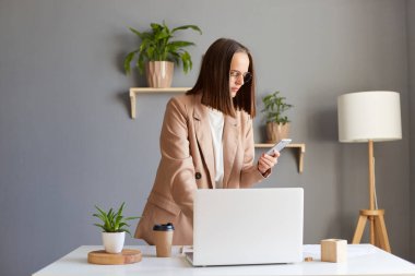 İş yerinin yanında elinde not defteriyle duran, elinde akıllı bir telefonla partnerini arayan, numarasını çeviren koyu renk saçlı serbest kadın portresi..