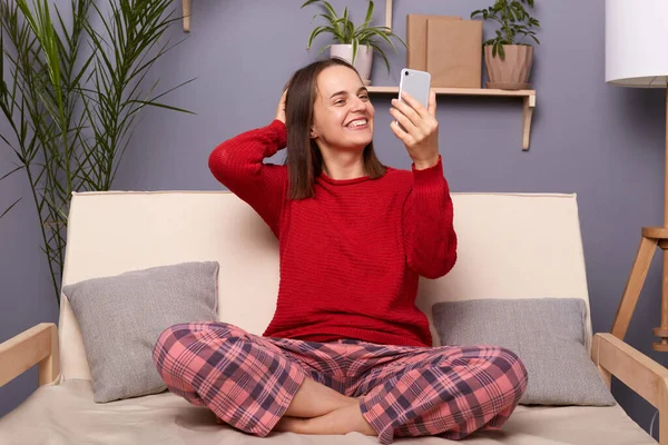 긍정적 스웨터를 체크무늬 바지를 소파에 스마트폰을 셀카를 비디오 전화를 — 스톡 사진