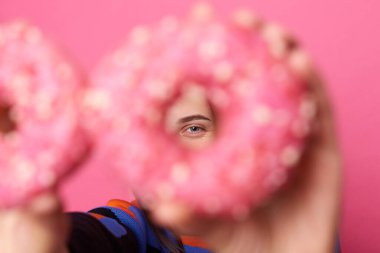 El ele tutuşan ve her ne kadar lezzetli görünse de kameraya parlak şekerlemeler serpiştirilmiş, pembe arka planda izole edilmiş bir kadın portresi..