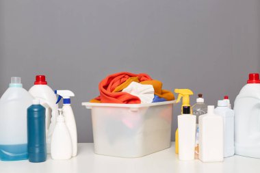 Kirli giysiler sepette. Masada deterjan, temizlik, çamaşırhane, temizlik, gri arka plan, temizlik ürünleri kapları, sıvı deterjan ve saç kremi..