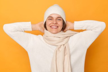 Sarı arka planda izole edilmiş sıcak süveter, kep ve eşarp giyen mutlu, genç bir kadının kapalı çekim, kollarını kaldırdı, keyifli bir ruh hali içinde.