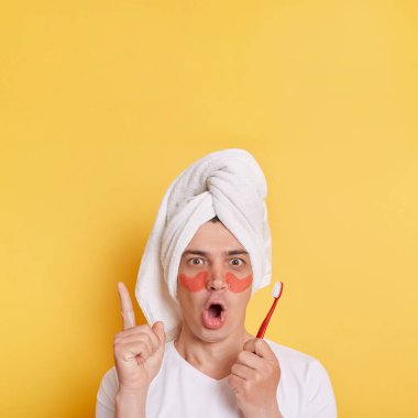 Göz altı yamalı, beyaz tişörtlü, havluya sarılı, sarı arka planda izole bir şekilde duran diş fırçası tutan, fotokopi çekilen.