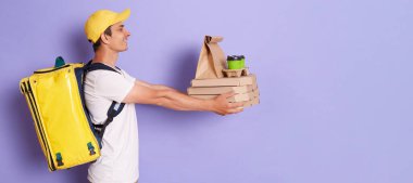 Yanında gülümseyen yetişkin kuryenin portresi pizza kutuları ve kahveleri tek kullanımlık bardaklarda tutarken mor arka planda izole edilmiş ellerde, müşteriye sipariş verirken, reklam için kopyalama alanı oluştururken..