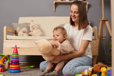 Erken eğitim ve gelişme. Sevgi dolu bir anne bebeğini kucağında tutuyor evde oyuncaklar oynuyor halının üstünde, mutluluk ve pozitif duyguları ifade ediyor..