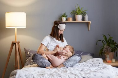 Yatakta bacak bacak üstüne atmış bir kadın portresi. Küçük bebeğini kucağında tutuyor. Evde oturup bebeğini emziriyor..