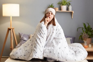 Uyku maskesi takmış, yorgana sarılmış, ağzı eliyle esneyen, uykusuz, uykusuz, uykusuz, uykusuz, uykusuz, uykusuz bir kadının kapalı bir çekimi..