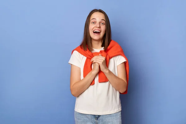 Portrait of amazed surprised woman wearing casual style clothing, keeps palms together, being surprised, looks happy, standing isolated over blue background.