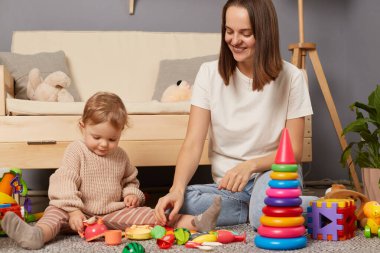 Image of smiling Caucasian smiling woman and daughter playing together while sitting on the floor at home. Activities with children inside, early childhood development