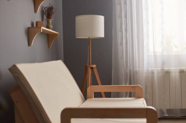 Image of cosy living room with gray wall and big window, shelf on wall, white cough near electric lamp, stylish home interior.