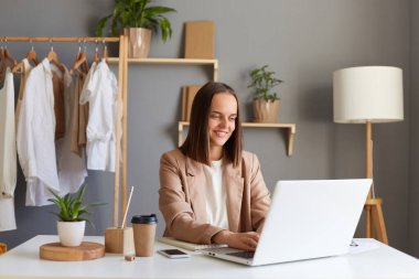 Ofiste poz veren, dizüstü bilgisayarda çalışan, klavyede daktilo kullanan, gülümseyen koyu renk saçlı güzel bir kadının portresi..