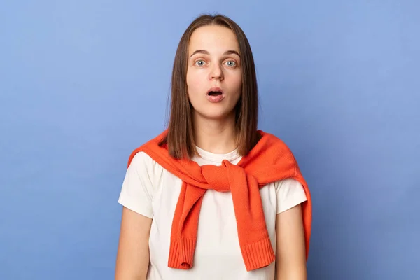 Photo of shocked amazed astonished, woman dressed white T-shirt and tied sweater over shoulders standing isolated on blue background, sees something surprised, looking at camera with big eyes.
