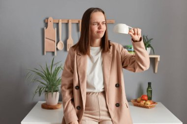 Tired and sleepy woman drinking coffee in the morning, feeling exhausted, suffering from insomnia and sleeping disorder, posing in kitchen, holding empty inverted cup.