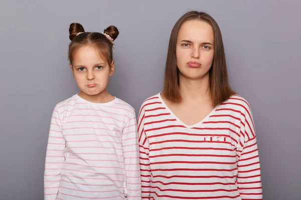 Image of sad upset family, mother and daughter wearing casual clothes, looking at camera with pout lips, expressing sorrow and sadness, standing isolated over gray background.