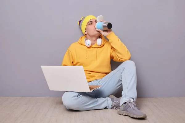 모자를 붙이고 노트북을 마루에 앉아서 로부터 마시고 목마른 사람의 — 스톡 사진