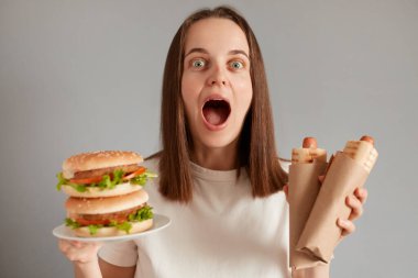 Beyaz tişörtlü, elinde hamburgerle sosisli sandviç tutan, diyetini bozan, fast food yiyen....