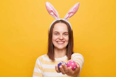 Paskalya yumurtalarını uzatan, bahar sembolü veren, sarı arka planda izole edilmiş sevimli, güler yüzlü bir kadın resmi..