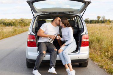 Romantik bir çiftin portresi yolda oturup öpüşmeleri, beyaz tişörtlü kadın ve erkeğin ülkeyi dolaşması, romantik bir yolculuk, otomobille balayı..