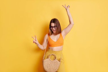 Son derece mutlu bir genç kadın portresi. Yazlık giysiler ve saman çantasıyla. Sarı üzerinde izole bir şekilde duruyor..