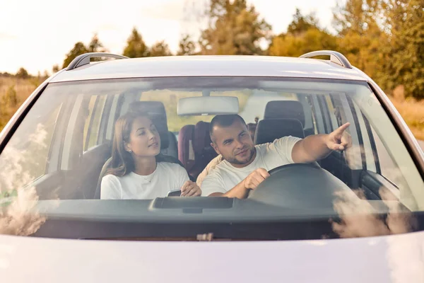 Couple driving in automobile, traveling around country, e sitting in the car, man pointing far away, showing interesting place to wife, enjoying their journey.