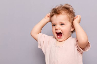 Gülen, şakacı, etkileyici, sevimli, sevimli, neşeli, komik saçlı kız çocuğunun portresi. Oynarken çığlık atan, iyi ruh halinde olan, bakışlarını çeviren, gri arka grond üzerinde izole bir şekilde duran, boşluğu kopyalayan..