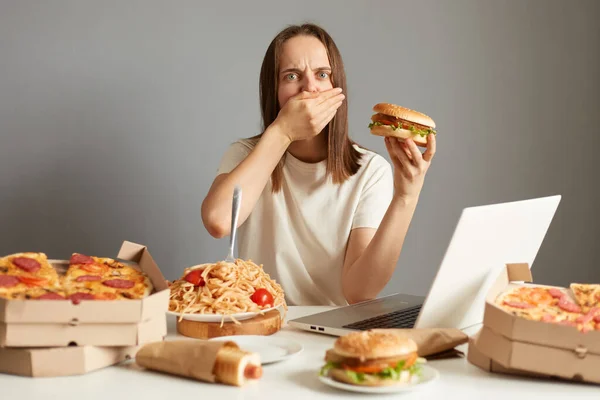 Retrato Mujer Enferma Comiendo Exceso Sentada Mesa Frente Cuaderno Aislado —  Fotos de Stock