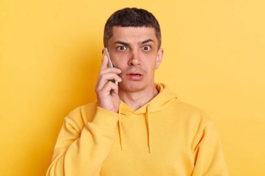 Şok olmuş, sıradan bir kapüşonlu adam telefonda konuşuyor. Haberleri duyunca şaşırdı. Büyük gözlerle kameraya bakıp sarı arka planda izole bir şekilde poz verdi..