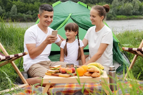 Семья Берегу Реки Рядом Палаткой Используя Смартфон Природе Отдых Открытом — стоковое фото