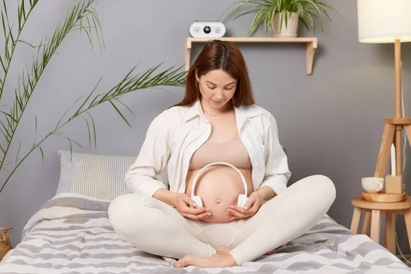 Hermosa Mujer Caucásica Morena Embarazada Sentada Cama Sosteniendo Auriculares Barriga — Foto de Stock