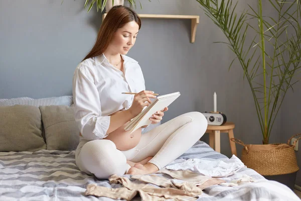 Vakava Vastuullinen Raskaana Oleva Nainen Valkoisissa Vaatteissa Istuu Sängyssä Paperisen — kuvapankkivalokuva