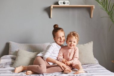 Gülümseyen kardeşler yatak odasında sarılıyorlar mutlu küçük kızlar yatakta oynuyorlar sabah mutlu bir şekilde gülüyorlar kameraya olumlu duygular izliyorlar..