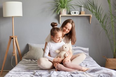 Anneler Günü. Kafkasyalı anne ve kız yatakta oturuyor tatlı çocuğuna sarılıyor gülümsüyor ve aile içinde olumlu duygular ifade ediyor..