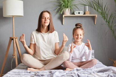 Meditasyon ve rahatlama. Genç bir anne ve küçük kızı Lotus pozisyonunda yatıyorlar, gözlerini kapalı tutuyorlar sabahları birlikte yoga yapıyorlar..