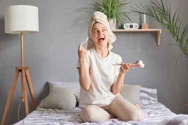 Son derece mutlu, yeni kozmetik pudralı göz gölgesi tutan havluyla aşırı mutlu genç bir kadın. Mutluluktan bağıran yeni kozmetik aletler..