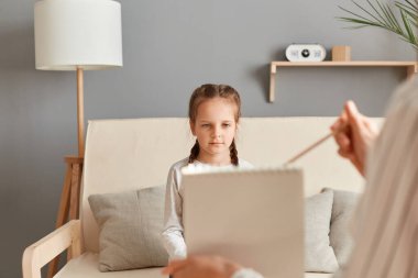 Çocukların psikolojik teşhislerinin modern yöntemleri. Ofisteki ruh sağlığını inceleyen kadın psikolog, küçük kız hastaya resmini gösteriyor..