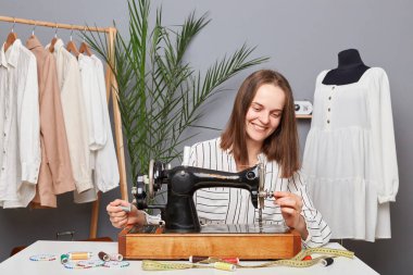 Beyaz, profesyonel, başarılı kadın tasarımcı, terzi terzi terzide dikiş makinesi dikiyor..