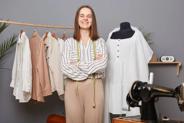 stock image Caucasian self-employed dressmaker woman at workplace work with textile for new fashion clothes collection in her sewing studio, standing with folded hands with confident expression.