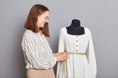 Gülümseyen, çalışkan kadın lağım mankeni, gri arka planda izole edilmiş yeni elbiseler, yeni elbise koleksiyonu hazırlayan moda giysiler..