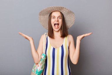 Uzun zamandır beklenen bir tatil. Çizgili mayo ve hasır şapka giyen heyecanlı mutlu kadın yaz uykusunda mutluluk çığlıkları atarak gri arkaplanı izole ediyor..