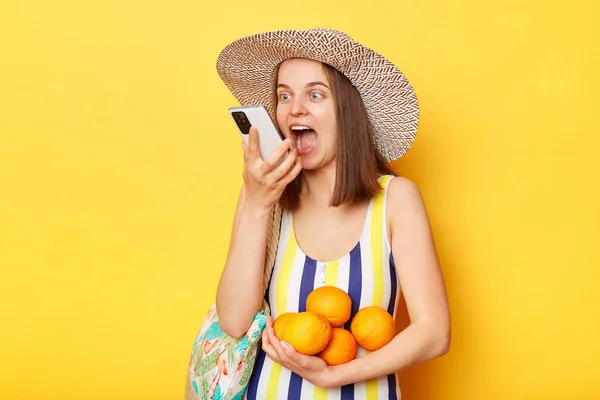 stock image Happy woman wearing striped swimsuit and straw hat isolated yellow background using smart phone recording voice message on summer vacation.