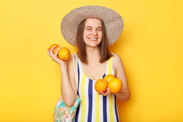 縞模様の水着と麦藁帽子を身に着けているかなり笑顔原因アジアの女性はオレンジのような夏の新鮮な果物を保持休憩を楽しんで黄色の背景を隔離 — ストック写真