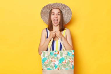 Dinlenen, çizgili mayo giyen, sarı arka planda izole edilmiş güneş şapkalı, yüzen ve güneşlenen, rahatlatıcı bir tatilin keyfini çıkaran,.