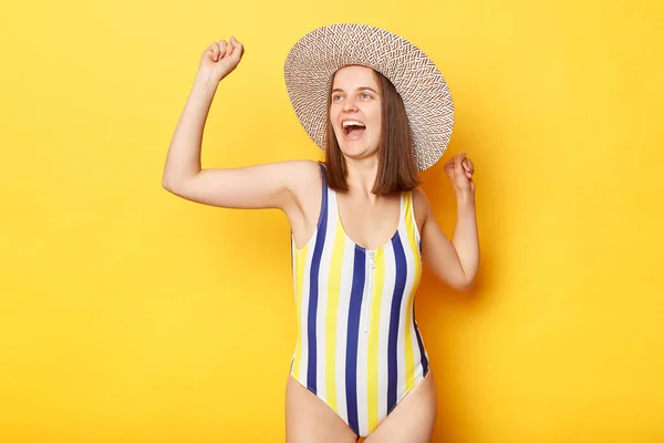 縞模様の水着と太陽の帽子を身に着けている非常に幸せな女性黄色の背景ダンス彼女の休暇を祝う 海で日光浴と水泳を楽しむ — ストック写真