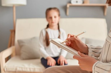 Psikolog, kadın çocukla seans yaparken notlar alıyor, duygusal ve zihinsel durumu hakkında önemli noktalar yazıyor, küçük kız sorunlarını dinliyor..