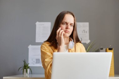 Dizüstü bilgisayarla çalışan, akıllı telefonla konuşan, üzgün duygularını ifade eden, ev ofisinden uzak duran, ortak ya da patronla iletişim kuran mutsuz, serbest çalışan kadın..