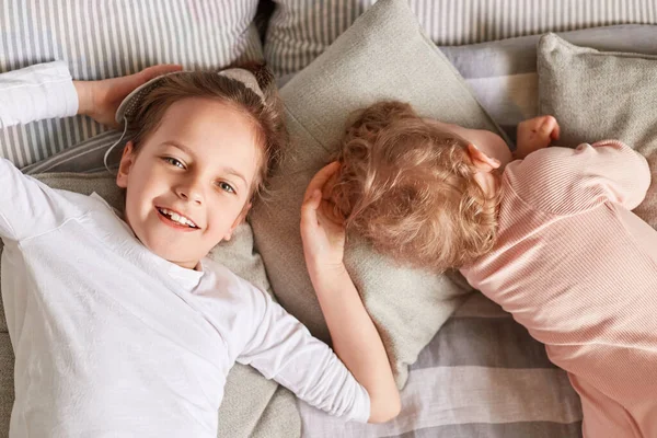 快乐的姐姐和小睡着的小宝宝一起躺在床上 在卧室里的兄弟姐妹们醒来 表达着积极的情感和快乐 — 图库照片