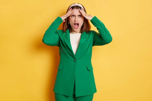 Despair shocked sad woman wearing green jacket standing isolated over yellow background screaming with negative emotions being depressed.
