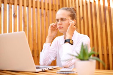 Beyaz tişörtlü, dışarıda bir kafede oturup dizüstü bilgisayar masajı yapan şablonlarla uğraşan yorgun bir kadın yeni iş tekliflerini düşünmekte zorlanıyor..